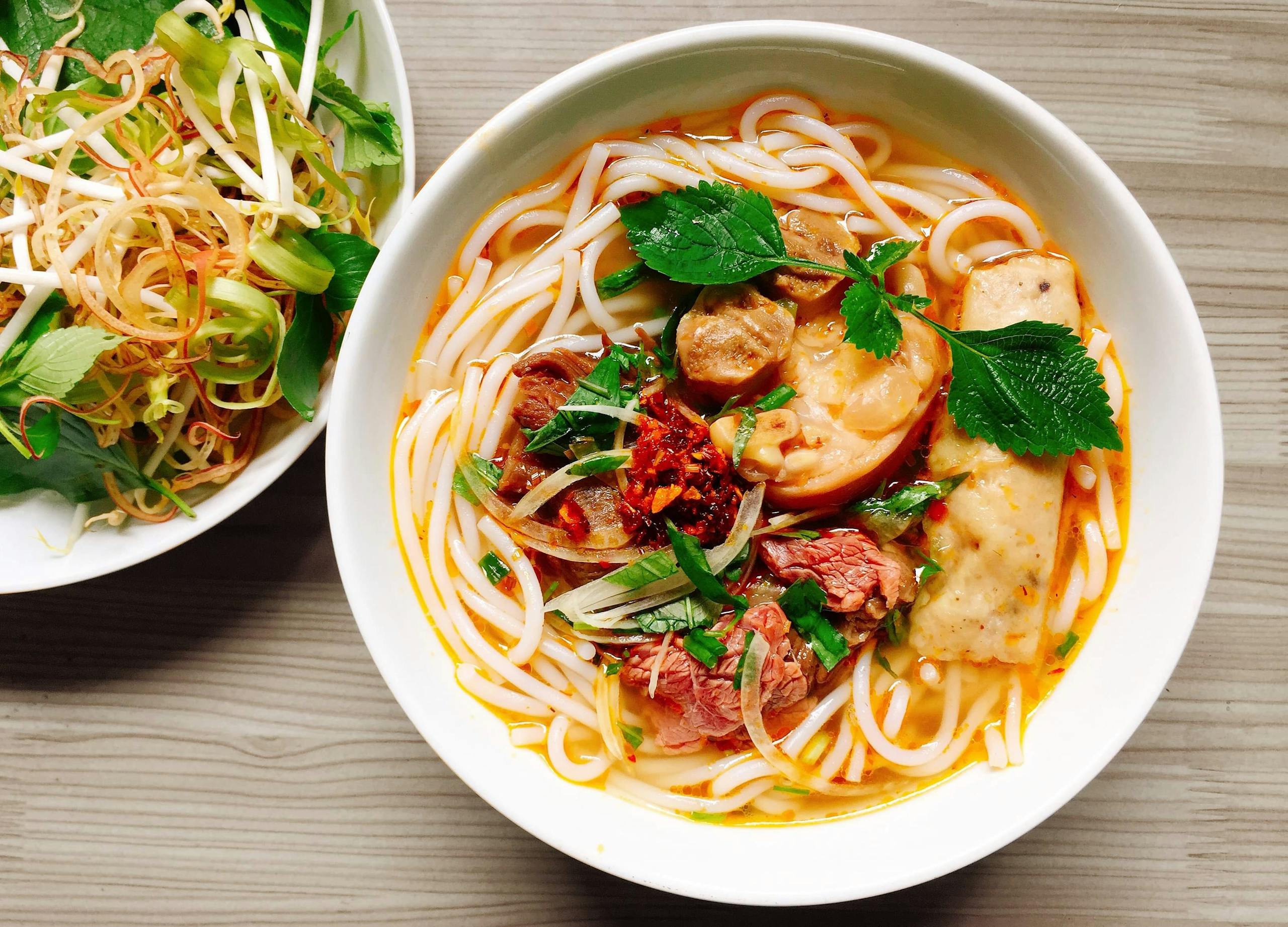 A colorful bowl of Vietnamese noodle soup with fresh herbs and vegetables.