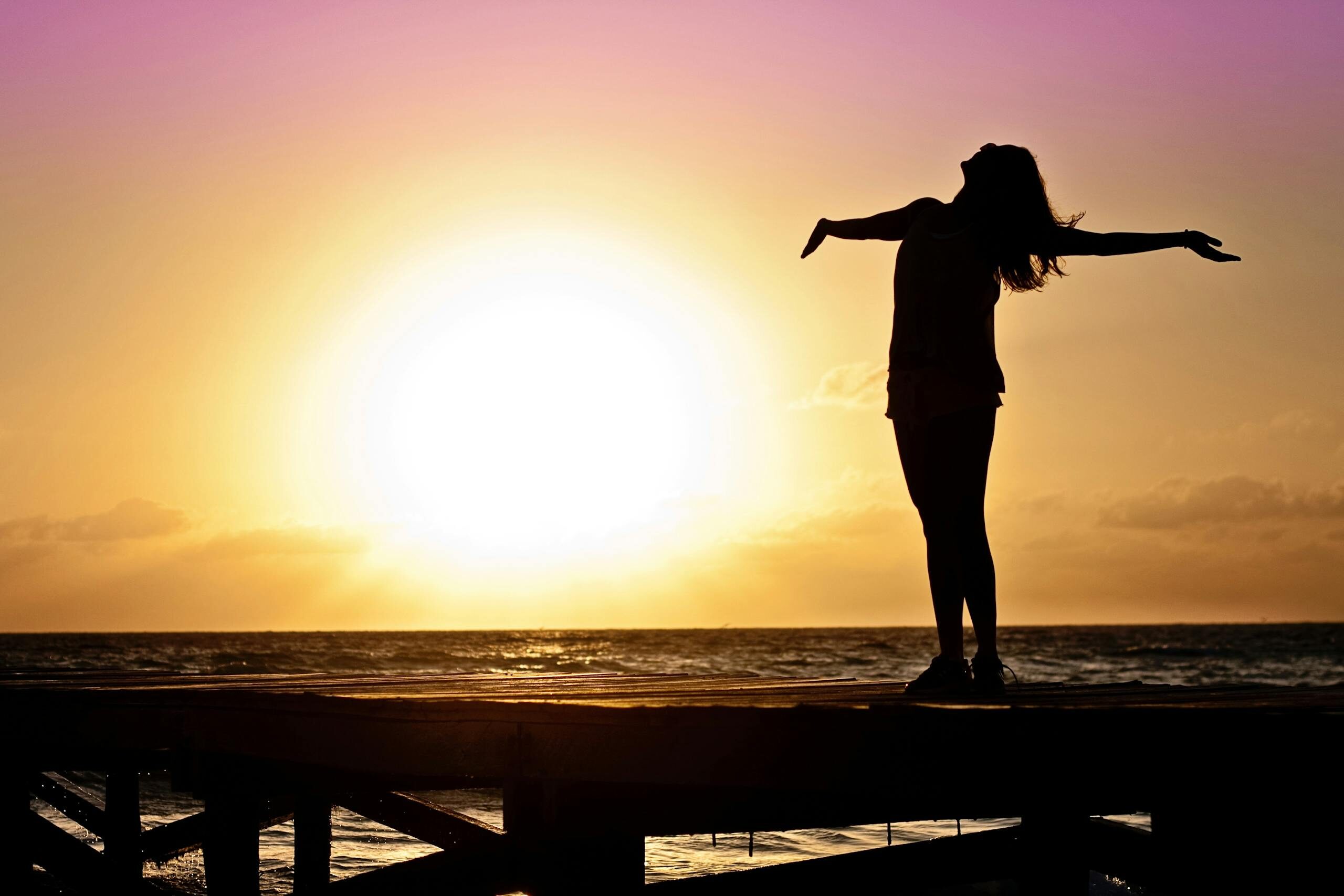 A joyful silhouette of a woman standing on a dock at sunset, embracing the freedom of nature.