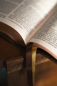 Close-up of an open Bible with ribbons on a wooden stand, warmly lit.