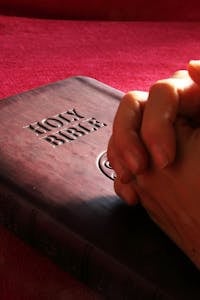 Close-up of hands praying on a Holy Bible, symbolizing faith and spirituality.
